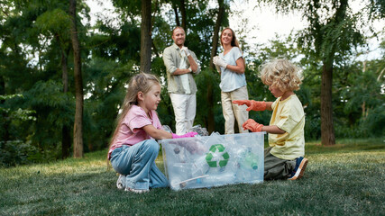 Children collecting plastic waste in forest or park with parents. Small brother and sister throwing plastic bottles into recycle bin