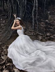 Russia, Moscow - 05/11/2020: Girl in a white long dress in the roots of trees.
