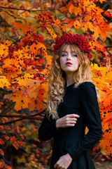 Beautiful girl in a black dress in a wreath of mountain ash in the autumn forest.