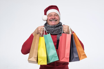 Surprised happy mature man in warm clothing holding paper bags. Studio shot