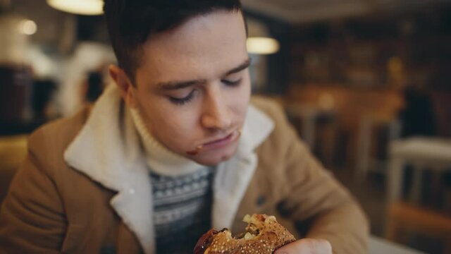 American style. Young man eating burger in fast food restaurant. People eat unhealthy meal. Getting satisfaction from unhealthy food. Junk food, modern life concet.