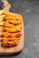 Vertical view of crispy and fried chicken meal on wooden cutting board on dark background
