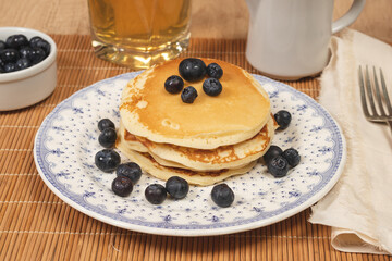 Stack of homemade pancakes prepared with blueberries and honey on an antique plate on a wooden table. Concept healthy food at breakfast.