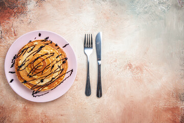 Stuffy pancakes decorated with chocolate syrup and fork and knife on a colourful table