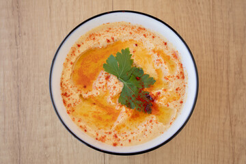 Top view of a Bowl with Hummus typical of Middle Eastern or Arab food with wooden background. Made with chickpeas, tahini, lemon and cumin forming a paste or cream. Concept of typical ethnic food.