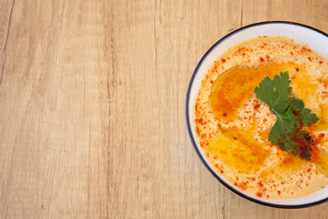 Top view of a Bowl with Hummus typical of Middle Eastern or Arab food with wooden background. Made with chickpeas, tahini, lemon and cumin forming a paste or cream. Concept of typical ethnic food.