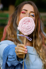 A beautiful girl with multi-colored hair and bright makeup with a lollipop in her hands coquettishly looks into the frame.