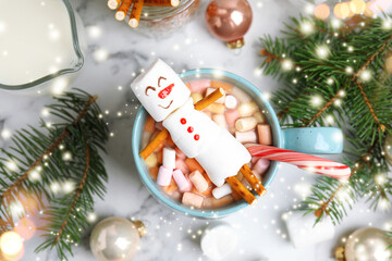 Flat lay composition with marshmallow snowman in cup of hot drink on white marble table. Bokeh...