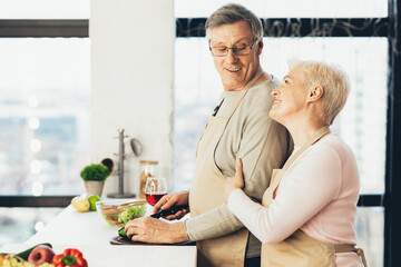 Elderly Couple Cooking Making Salad For Dinner In Kitchen, Side-View