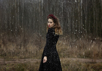 Russia, Moscow - 11/14/2020: a beautiful girl with curly blond hair stands in a black dress looking at the camera, it is snowing.