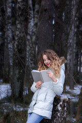 A girl with a book stands in the forest and reads. Snowing.
