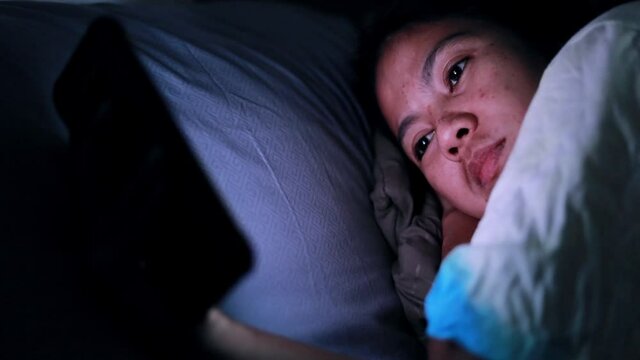 Asian woman sleeps late using a smartphone in the dark at the bed