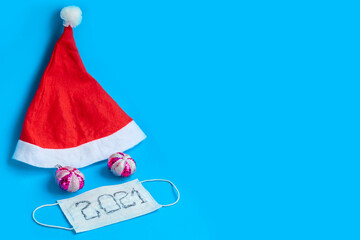 Red Santa Claus cap and medical mask on a blue background, ban on mass celebrations in the New Year and Christmas, minimalistic New Year's concept