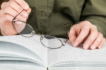 A woman holds black-rimmed glasses against the background of an open textbook reading books in...