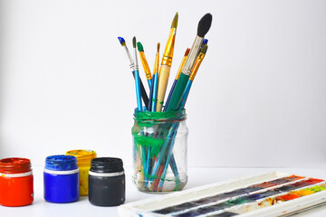 paint brushes in a glass jar. Painting brushes and gouache on white background