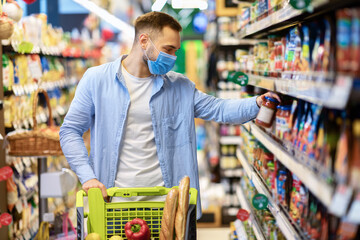 Young man in face mask with cart shopping in hypermarket