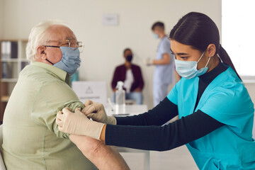 Woman doctor nurse in medical uniform and protective mask making vaccination senior elderly man