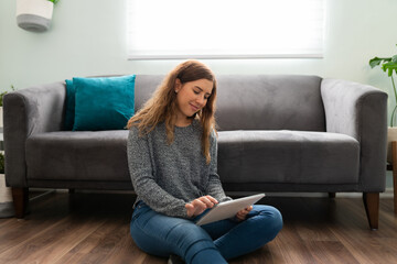 Obraz premium Smiling woman in her 20s using her touch screen in her lounge