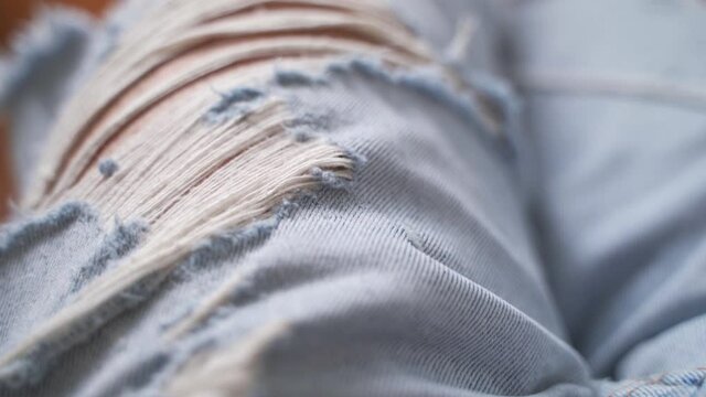 close up texture of ripped blue jean on person. faded and torn denim for background.