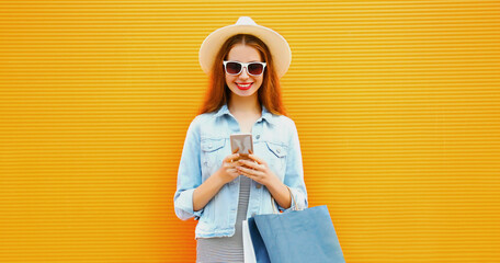 Close up of young woman with smartphone and shopping bags wearing a summer straw hat over an orange background