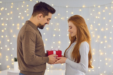 Young happy smiling couple standing and giving presents during celebrating holiday at home