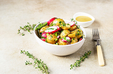 Tasty hot potato salad with green beans, fresh radishes and herbs dressing with olive oil and mustard sauce, light background.