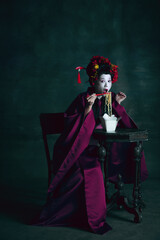 Tasty fastfood. Young japanese woman as geisha isolated on dark green background. Retro style, comparison of eras concept. Beautiful female model like bright historical character, old-fashioned.