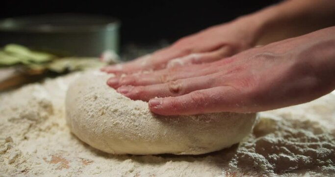 Chef forming the dough on a floured surface and kneading it with his hands, in a traditional pizzeria kitchen. Pizza maker prepares the dough for a gluten free pizza. Close up. Shot in 6K