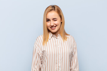 young blonde woman looking happy and friendly, smiling and winking an eye at you with a positive...