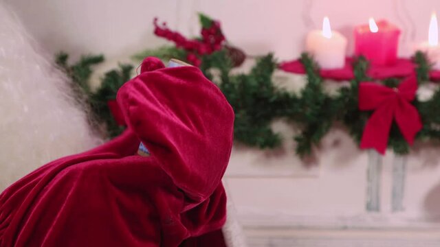 Santa Claus's hands in red mittens blow up a clapperboard close-up. Candles are burning, a green branch with red bows. Traditional preparation before the new year. Holiday greetings for the family.