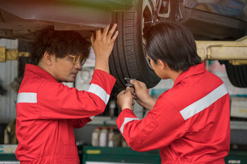 Technicians team to fix cars, wear red uniforms, use tools to measure tires in the garage.
