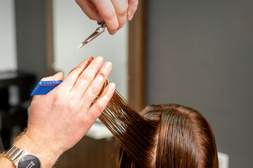 Close up of male hairdresser's hands cuts female hair in a hair salon. Selective focus