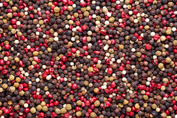Surface covered with multiple red, black and green pepper seeds as a background texture composition