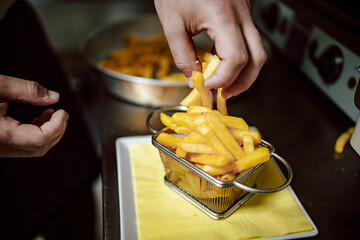 Close-up of chef hands arranging fries in small metal basket in the restaurant