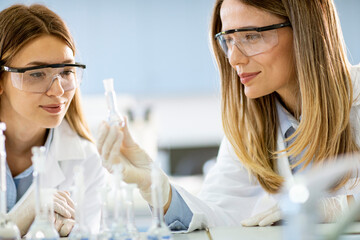 Two female scientific researchers looking at a flasks with solutions in a laboratory
