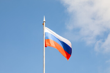 The flag of the Russian Federation flutters in the wind against the blue sky