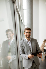 Young businessman standing with digital tablet by the office window