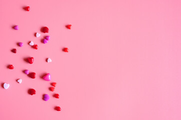 a heap of heart shaped glossy beads in different pink shades on a pink background. space for text