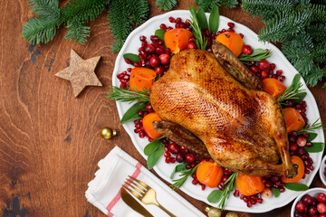 Christmas oven roasted duck on a white plate decorated with cranberries, pomegranate, persimmon, rosemary and sage.  Copy space. Chrismas food concept. © Olga Romankova