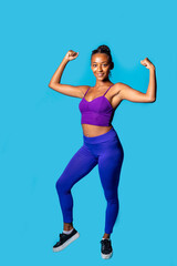 Fit young black woman showing muscle on blue background powerful gesture smiling
