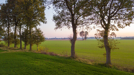 Obraz premium Dramatic and colorful sunrise or sunset sky over a grassy green farmfield shot from drone high up. High quality photo