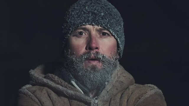 Man with frozen face. Young adult man with icy beard and hat breathes outdoor at subzero temperatures environment