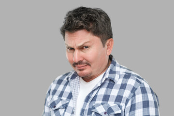 Obraz premium closeup portrait of serious handsome middle aged business man in casual checkered shirt standing and looking at camera with doubtful face. indoor studio shot, isolated on gray background.