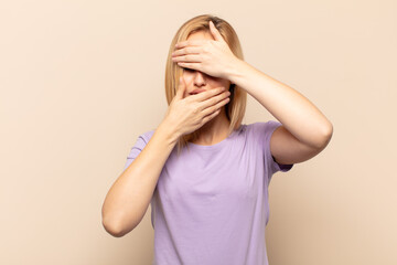 young blonde woman covering face with both hands saying no to the camera! refusing pictures or...