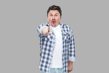 Portrait of shocked handsome middle aged business man in casual checkered shirt standing, pointing and looking at camera with unbelievable face. indoor studio shot, isolated on gray background.