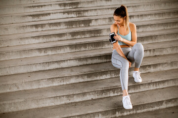 Fitness woman taking a break from running sitting on steps and suing mobile phone in armband