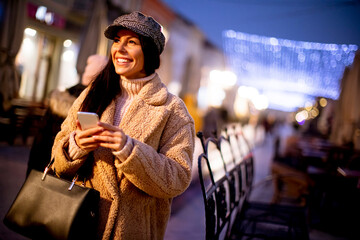 Pretty young woman using her mobile phone in the street at Christmas time