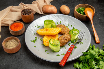 Side view of cutlet meal potatoes different spices and geens with towel on dark table