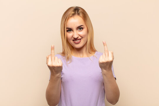 young blonde woman feeling provocative, aggressive and obscene, flipping the middle finger, with a rebellious attitude