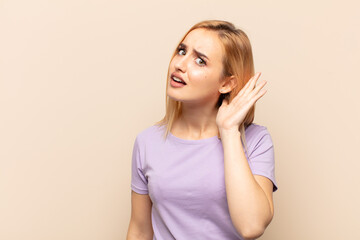 young blonde woman looking serious and curious, listening, trying to hear a secret conversation or...